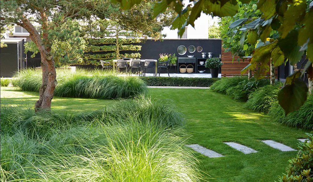 Gepflegte Gartenanlage mit Rasenfläche, Ziergräsern und Trittplatten